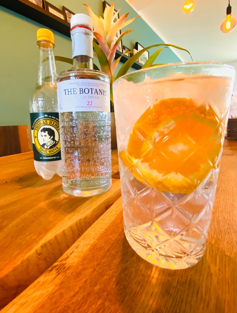 Im Vordergrund der fertige Gin Tonic mit The Botanist Gin und Thomas Henry Tonic Water 